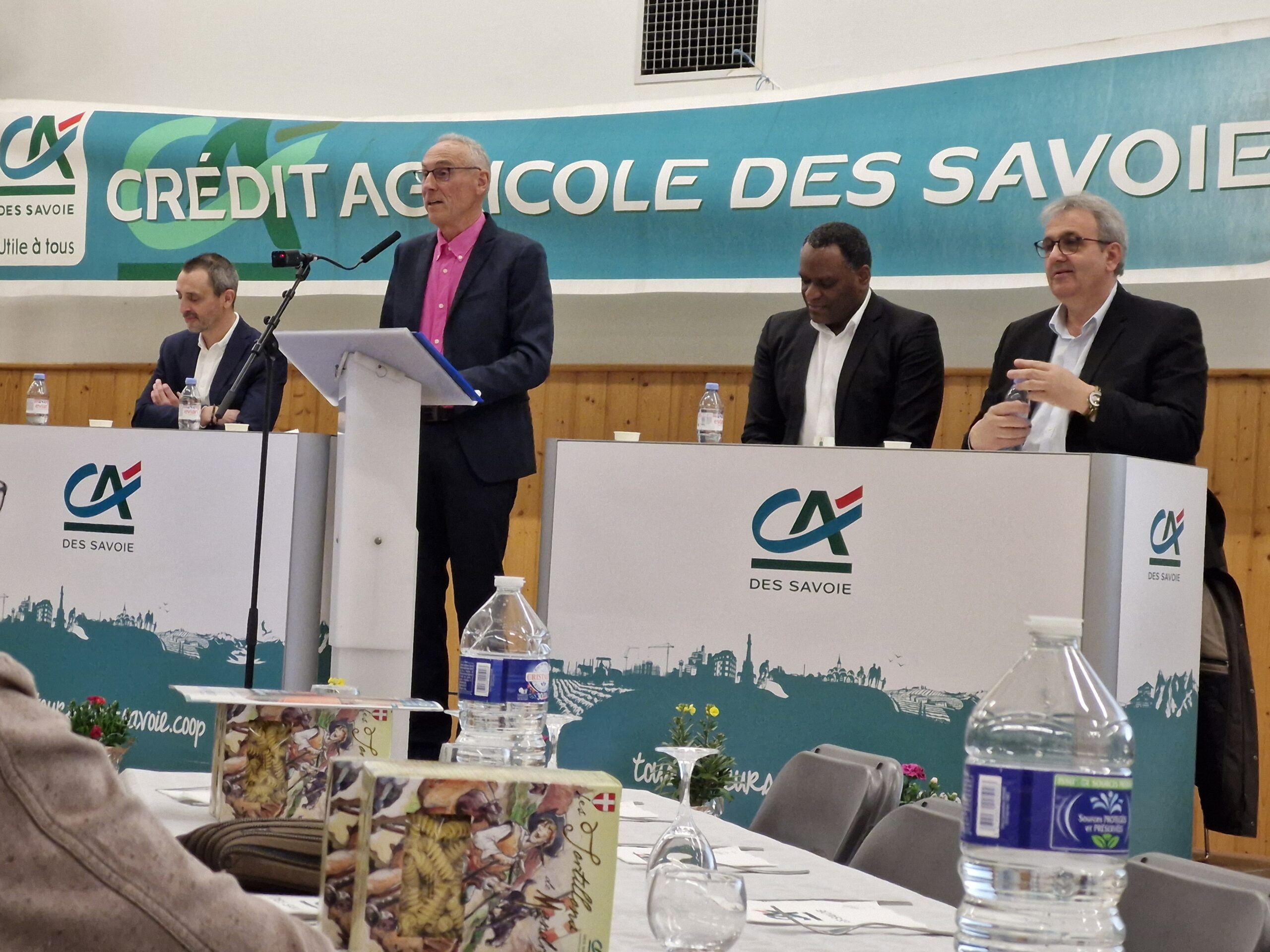 Sur scène, derrière des bureaux, des représentants du Crédit Agricole des Savoie, dont une prenant la parole derrière le pupitre.