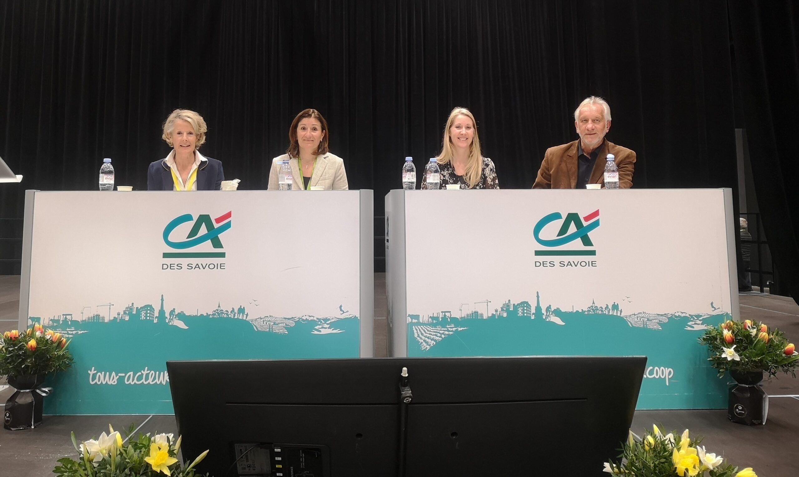 Sur scène, 4 personnes derrière un bureau.