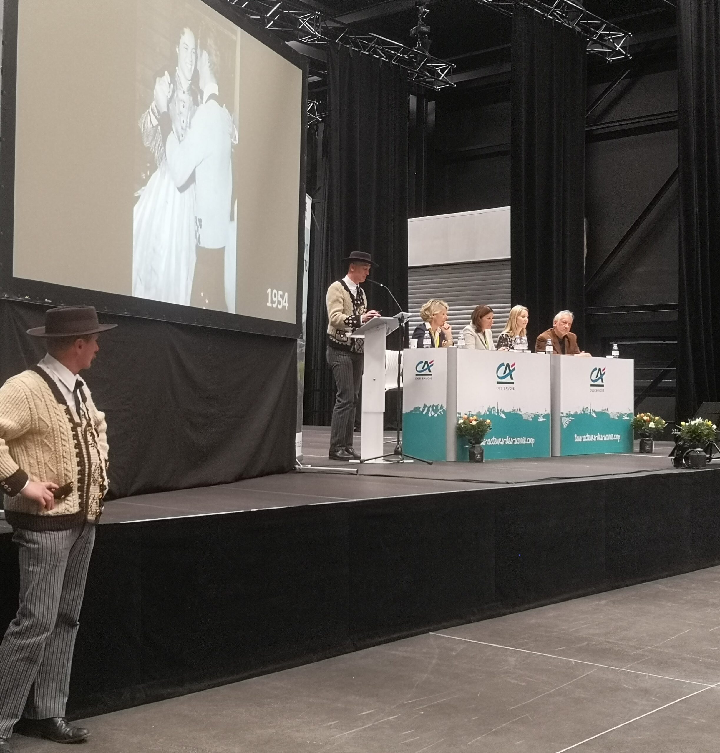 Sur scène, 4 personnes derrière un bureau, 1 personne en tenu traditionnel.