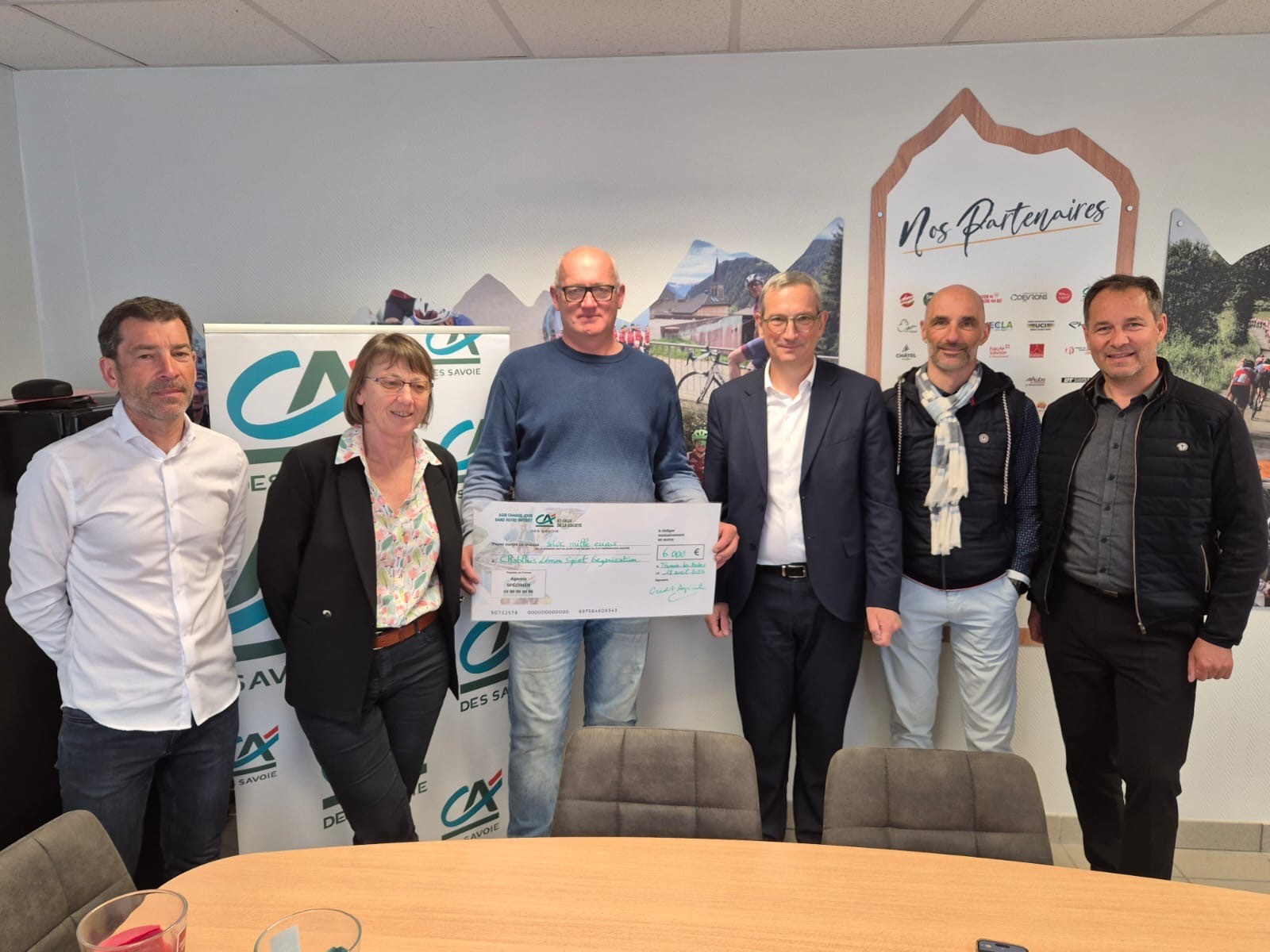 Remise du chèque pour le partenariat des courses de cyclisme. Six personnes se tiennent debout, l'une avec le chèque.